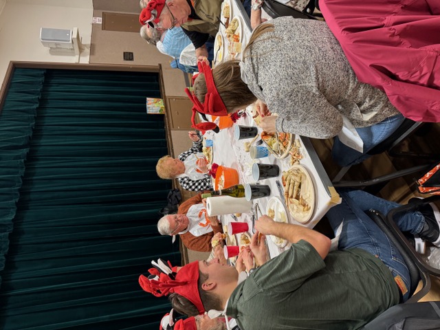Yachats Lions Club - Crab Feed 2024; another view of a table of crab-eaters in front of the stage